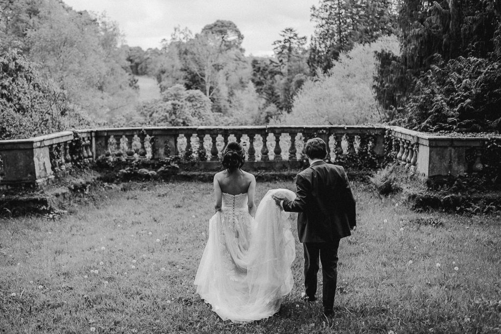 bride and groom walking as groom holds bride dress.
