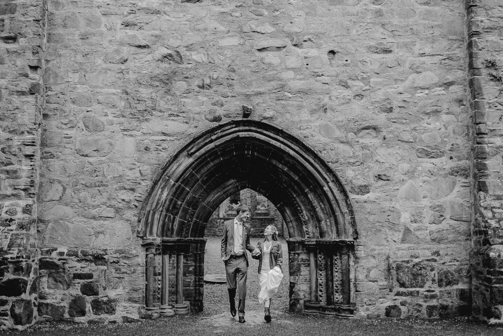 bride and groom walk out under arch 