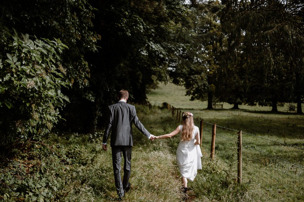 bride and groom walk hand in hand in field 