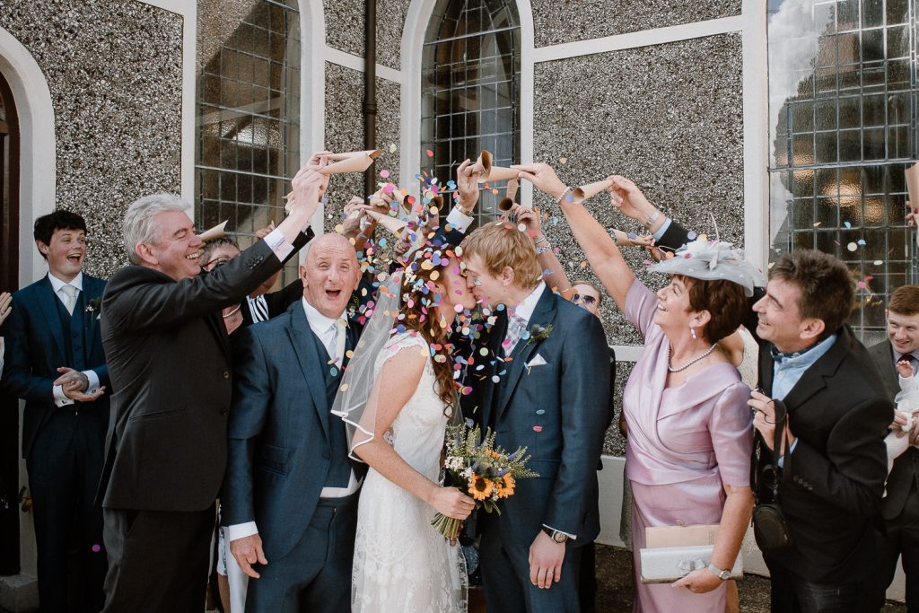 guests throw coloured confetti over bride and groom
