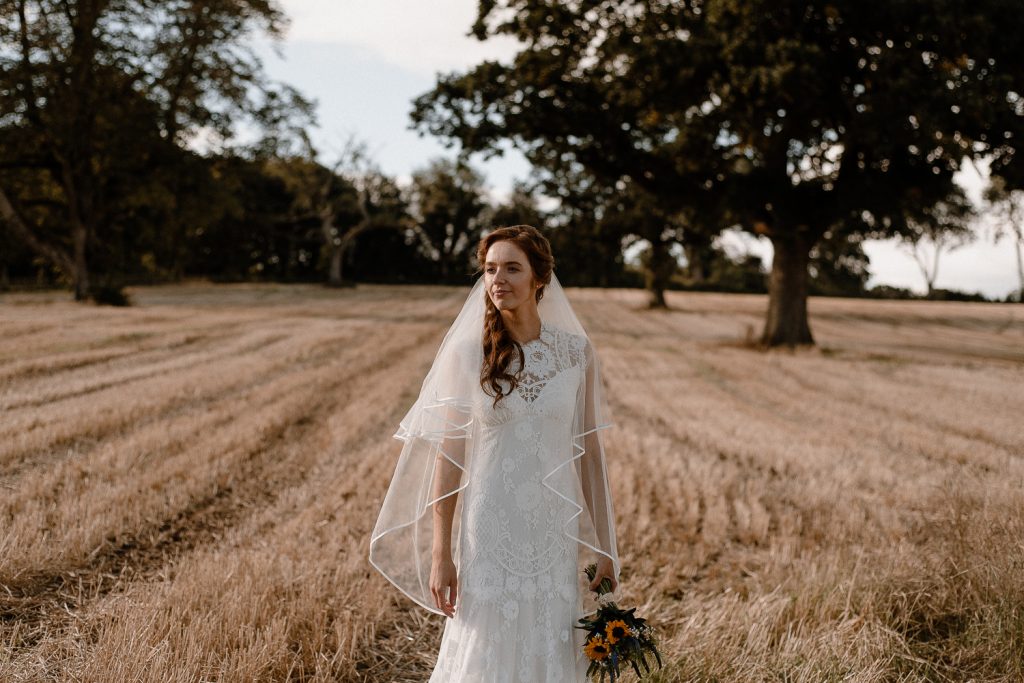 bride stands alone in field. Gracehall wedding