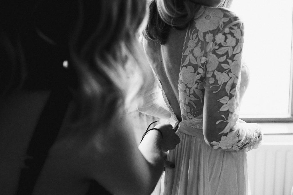 close up of sister doing back of brides dress 