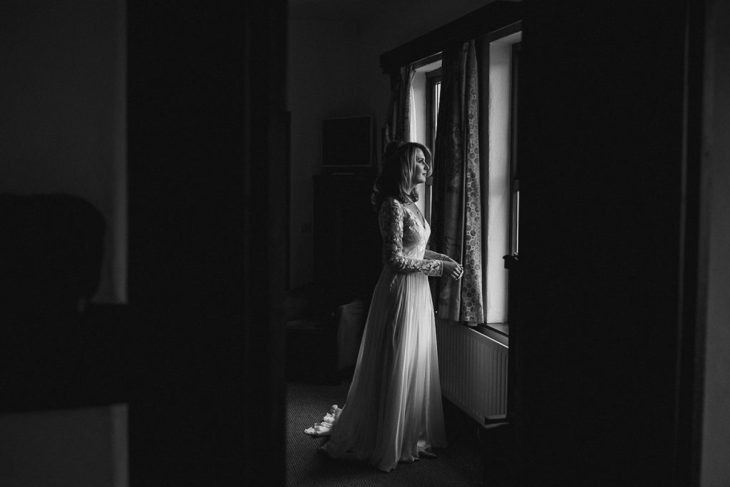 bride standing alone in wedding dress in soft window light