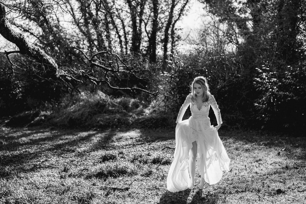 bride lifting her dress to walk though a muddy field 