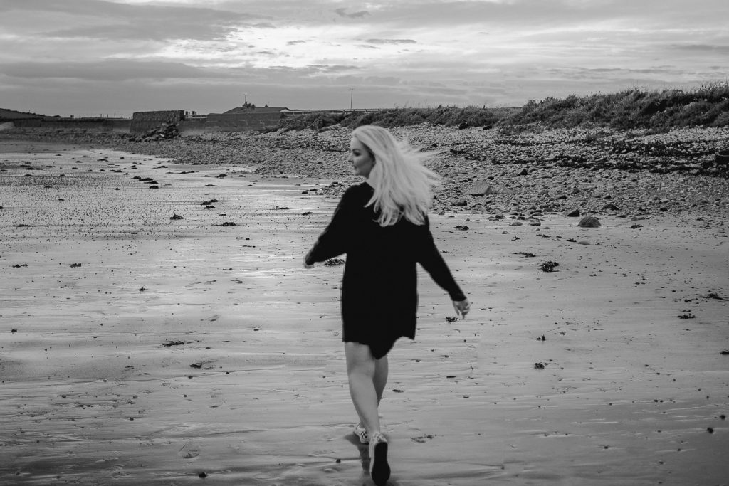 woman with blond hair and black dress running on beach 