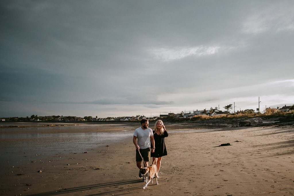 couple walking on beach with dog at sunset 