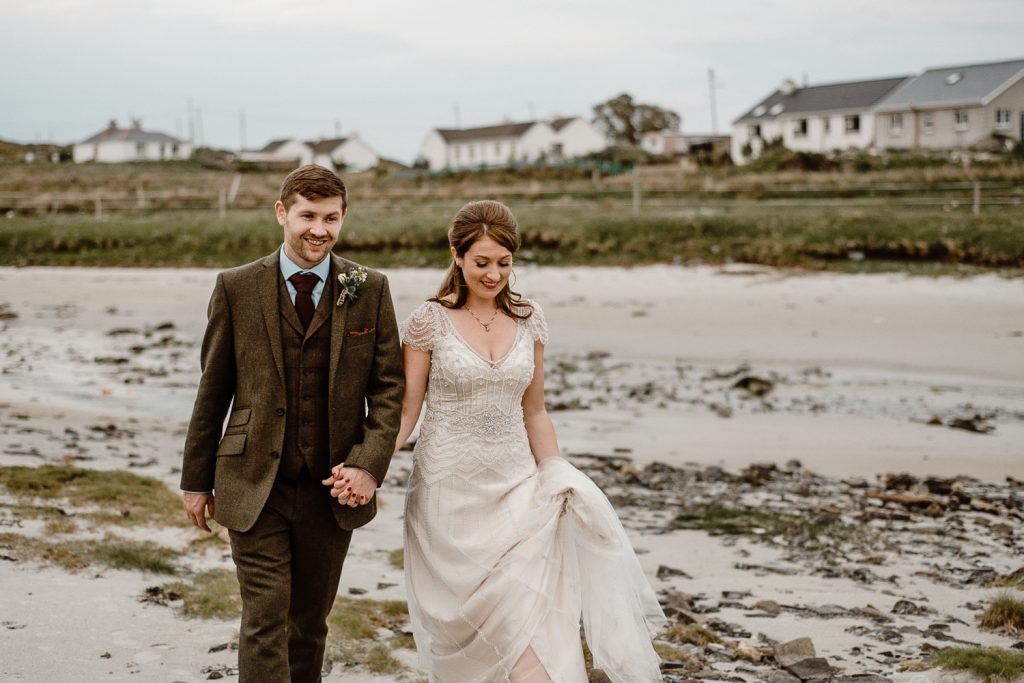 bride and groom holding hands walking on beech behind dawros bay house donegal 