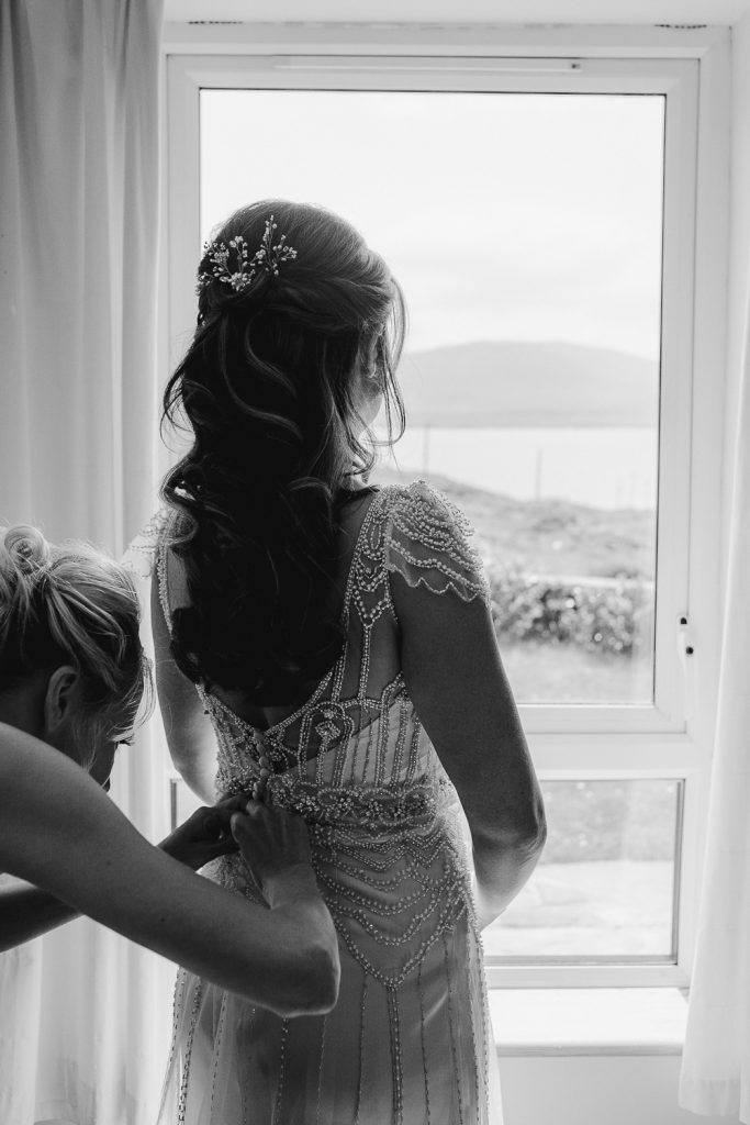 bride getting back of dress zipped at window 