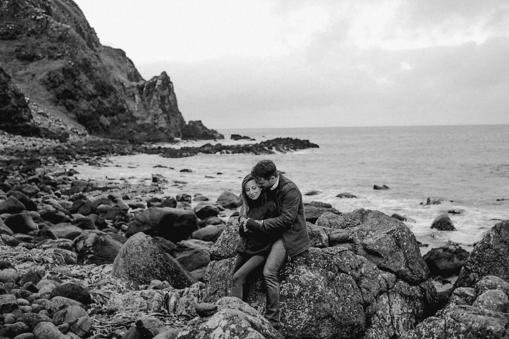 couple sitting on rocks at beach hugging 