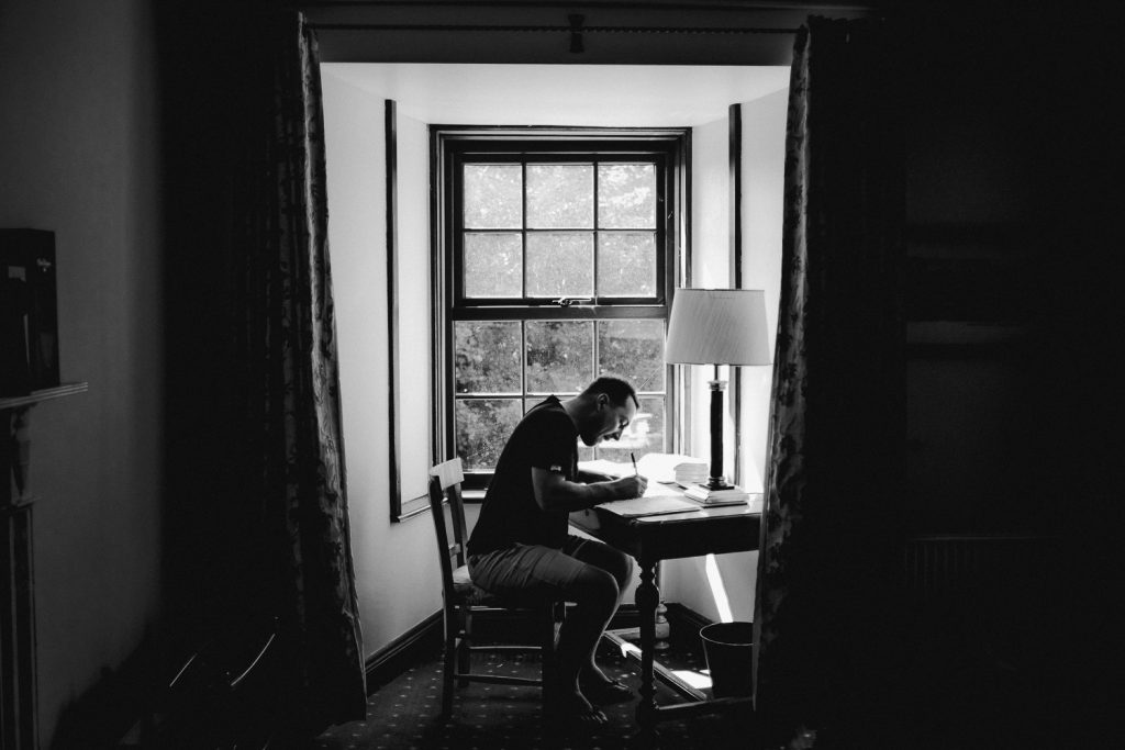 Groom writing speech at window light